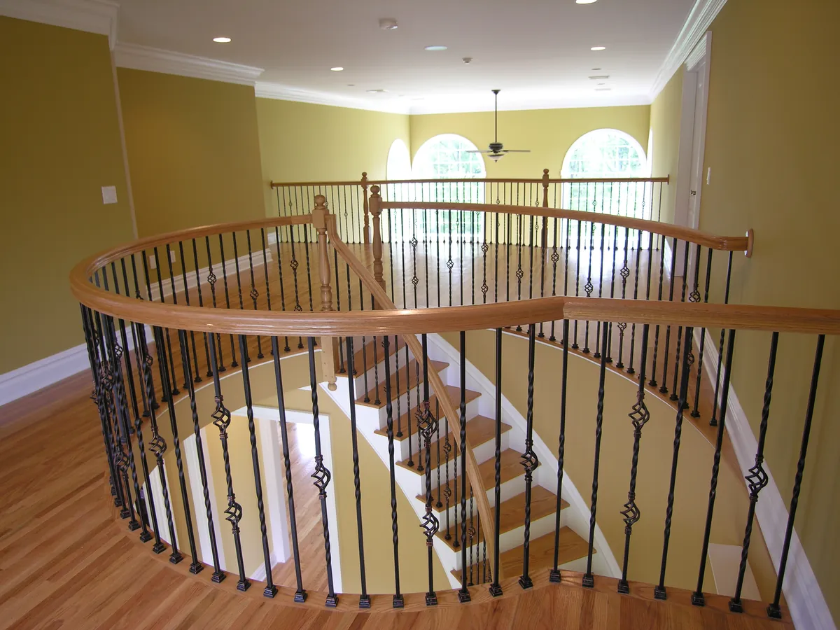 Curved upper-landing balcony with wrought-iron balusters and a red oak handrail installed by Snyder Stairs in the Lehigh Valley
